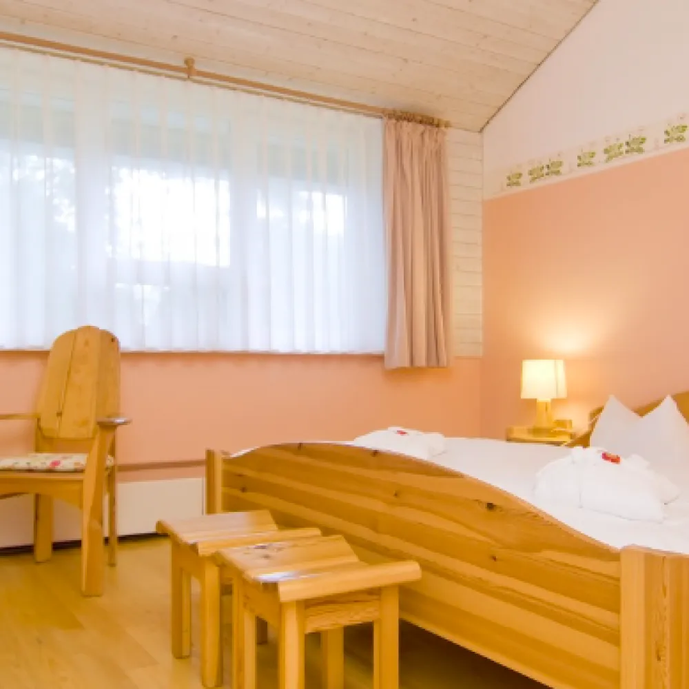 Doppelzimmer in zartem Rosa mit Holzbett und Sessel
